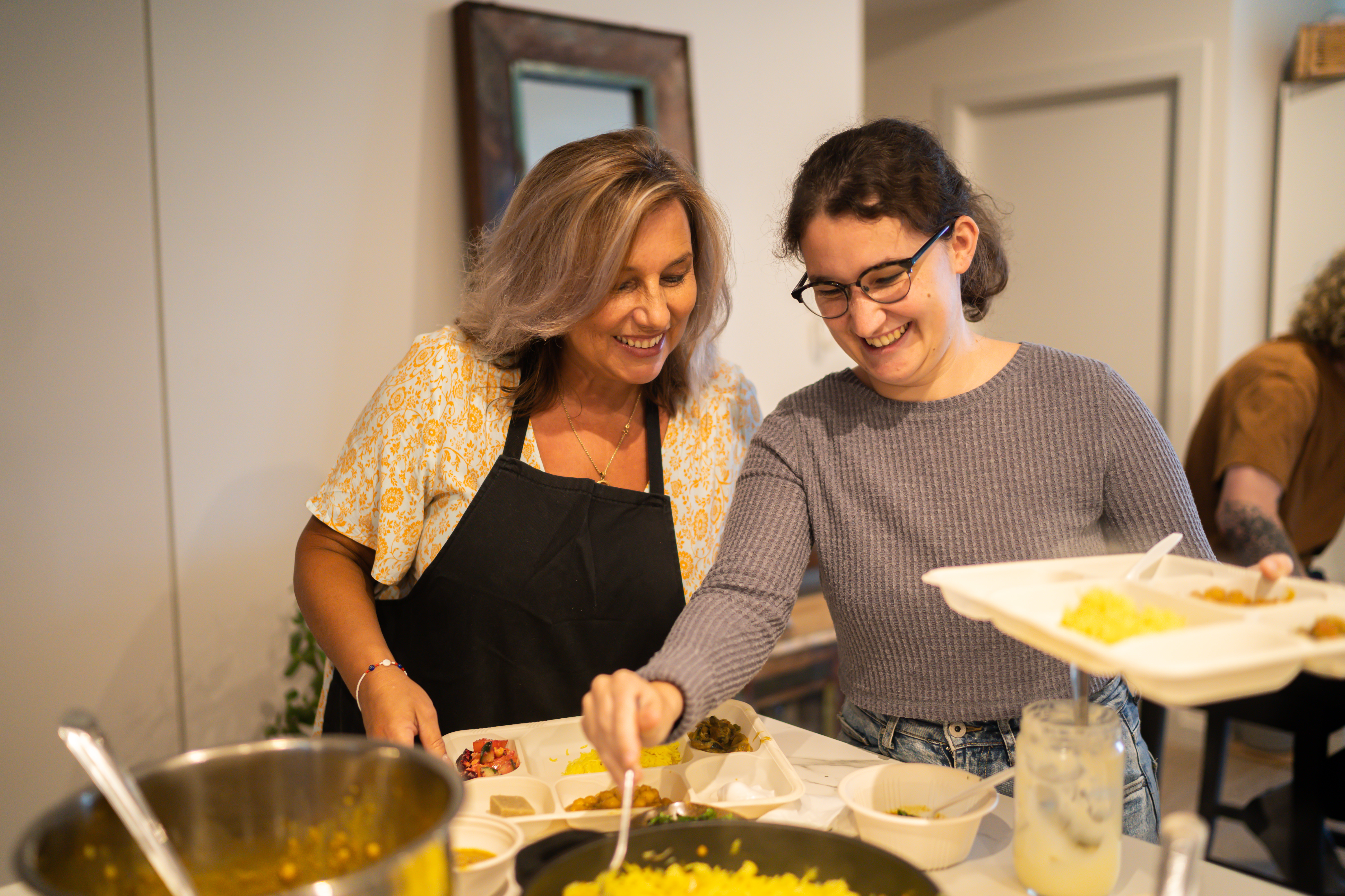 Two women laughing while plating up vegan food onto trays